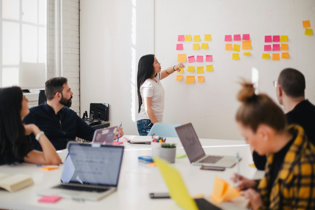 group of workers in a room with laptops and post-it notes on the wall